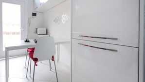 Een moderne keuken met witte kasten, een magnetron, en een eethoek met een witte tafel en rode stoelen.