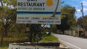 A sign for Playa Paradise Bar Restaurant with contact information and a welcome message.