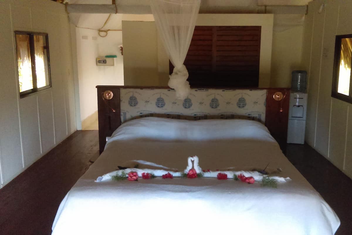 Een netjes opgemaakt bed met een decoratieve zwaan en bloemen, een houten hoofdbord en een klein nachtkastje met een waterdispenser.