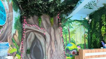 Habitación con un mural de un árbol y bosque, una mesa de recepción y una mesa con un jarrón de flores.