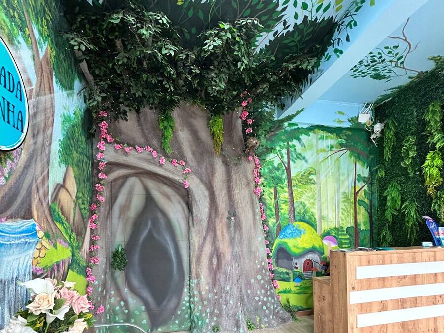 Et værelse med et mural af et træ og en skov, en receptionsdisk og et bord med en vase blomster.