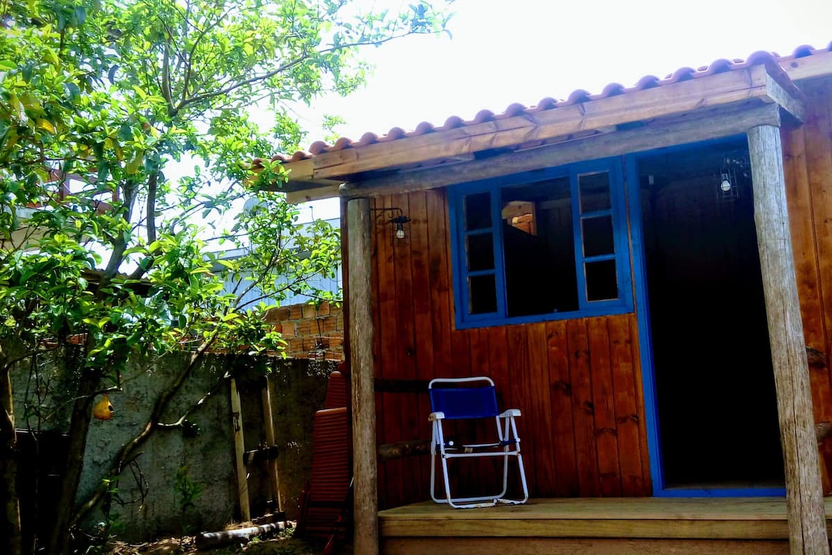 A wooden house with a blue door and windows, a red chair outside, and a tree in the background.
