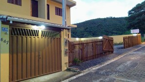 Una entrada cerrada con un portón metálico y valla de madera, un letrero que indica una propiedad llamada "Paseo de Ajuda", y un paisaje montañoso al fondo.