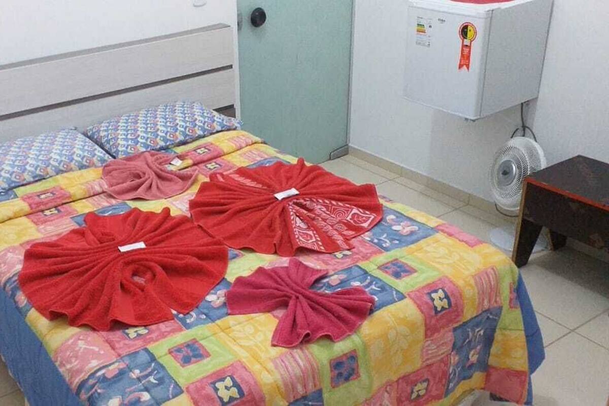 A room with a bed, a wooden stool, a wall-mounted air conditioner, and a fan.