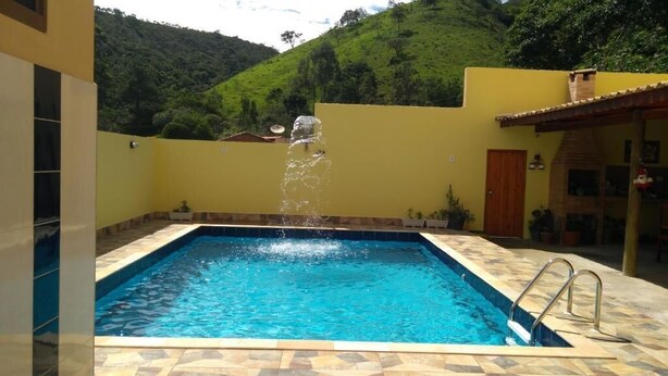 Una piscina con una fuente de agua, rodeada por una terraza con baldosas y una pared amarilla.
