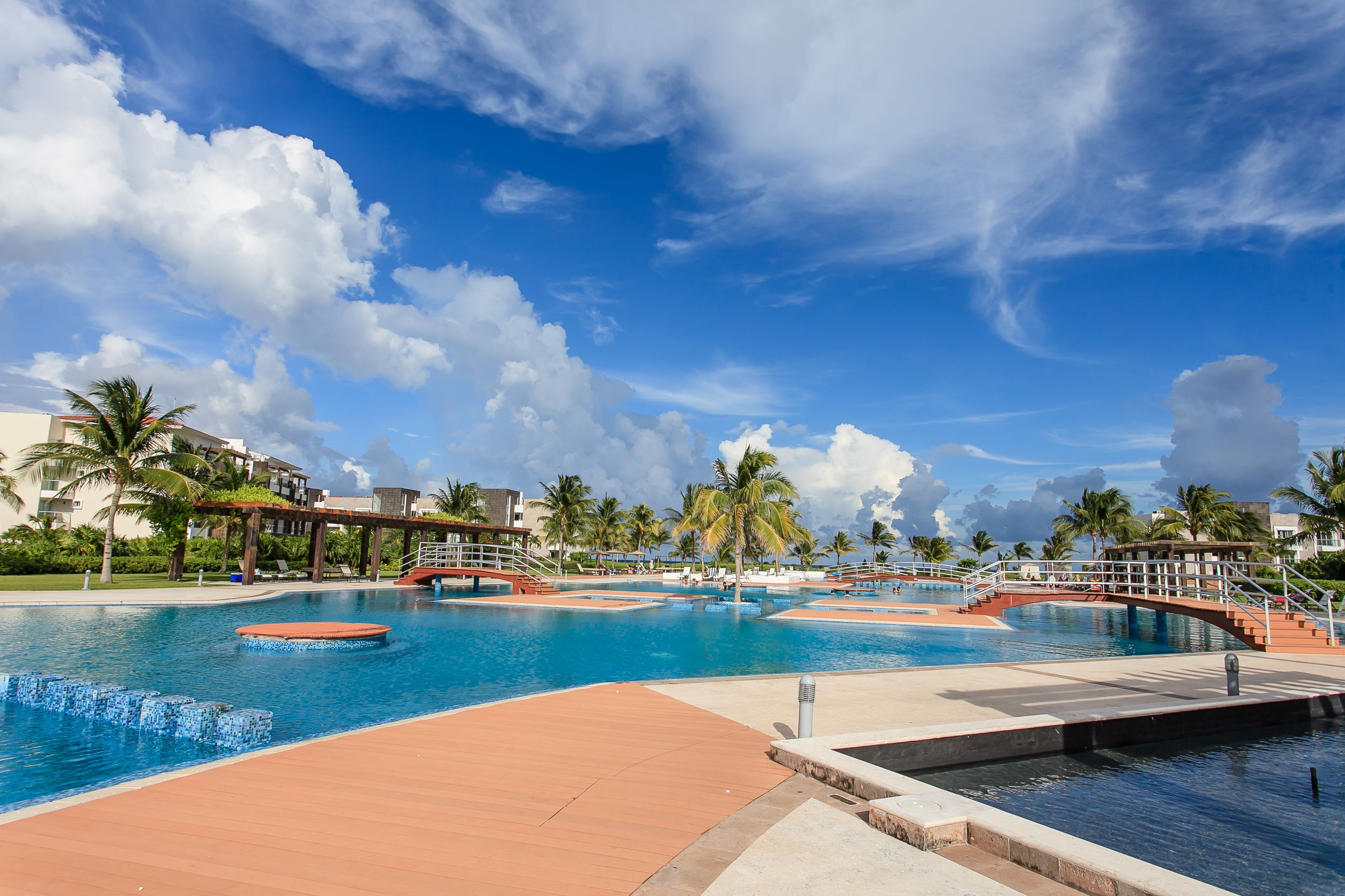 A large outdoor swimming pool with multiple sections, palm trees, and a bridge connecting different areas.