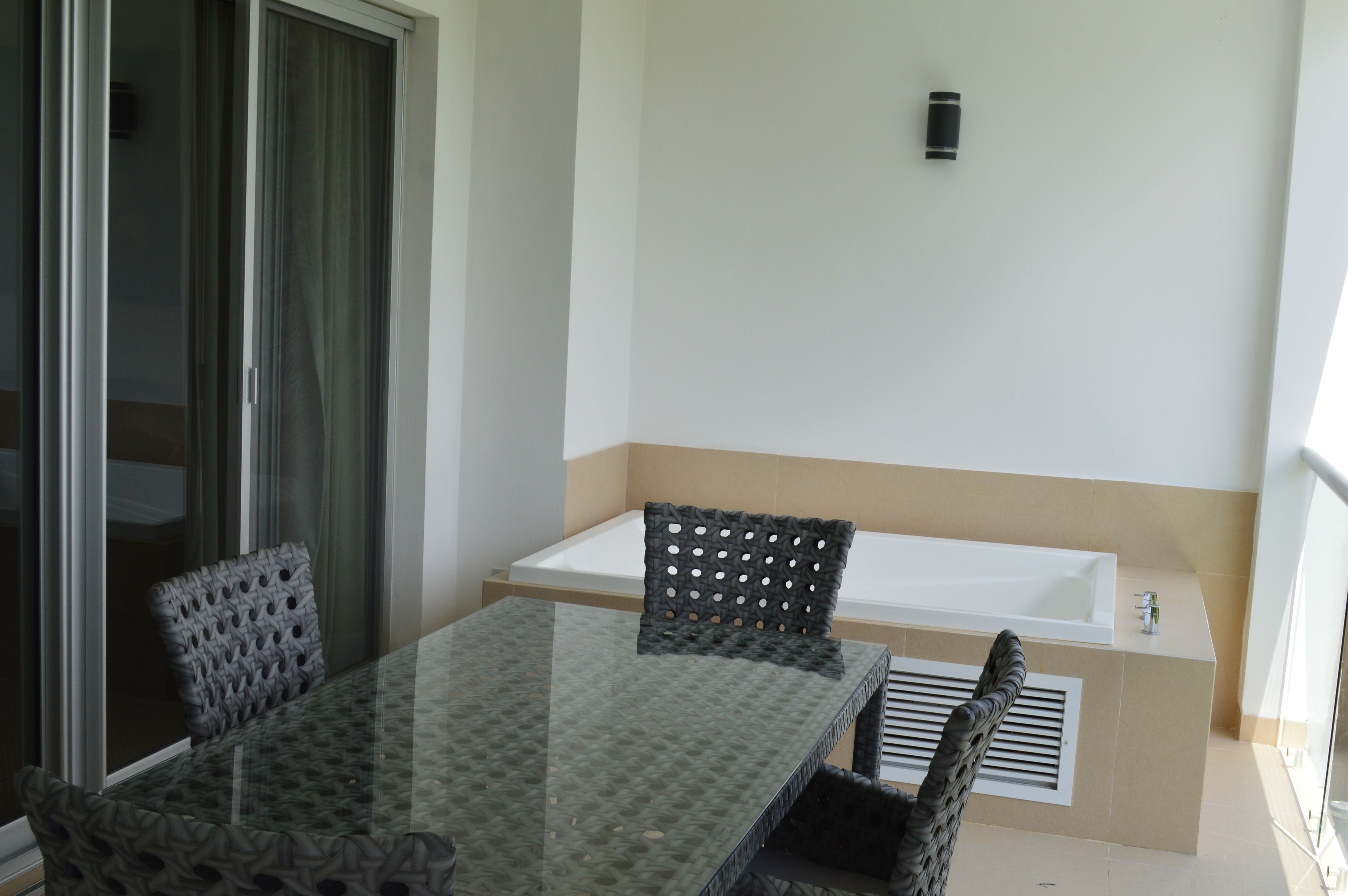 Un balcon avec une table et des chaises en verre, une baignoire blanche et une porte-fenêtre coulissante.