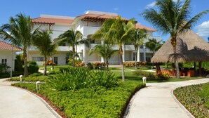 Een resort met een wit gebouw, palmbomen en een constructie met rieten dak.