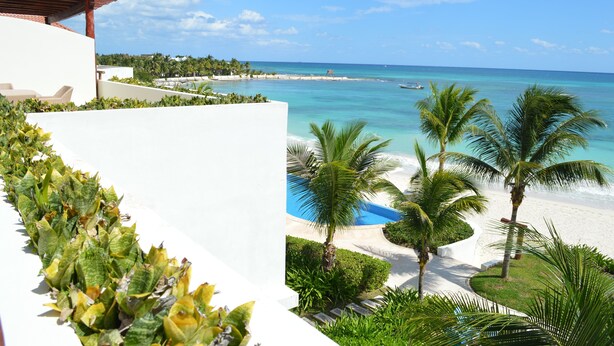 Een resort met een wit gebouw, een strand en palmbomen.