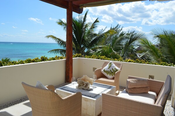A balcony with wicker furniture, a table with a decorative centerpiece, and a view of the ocean.