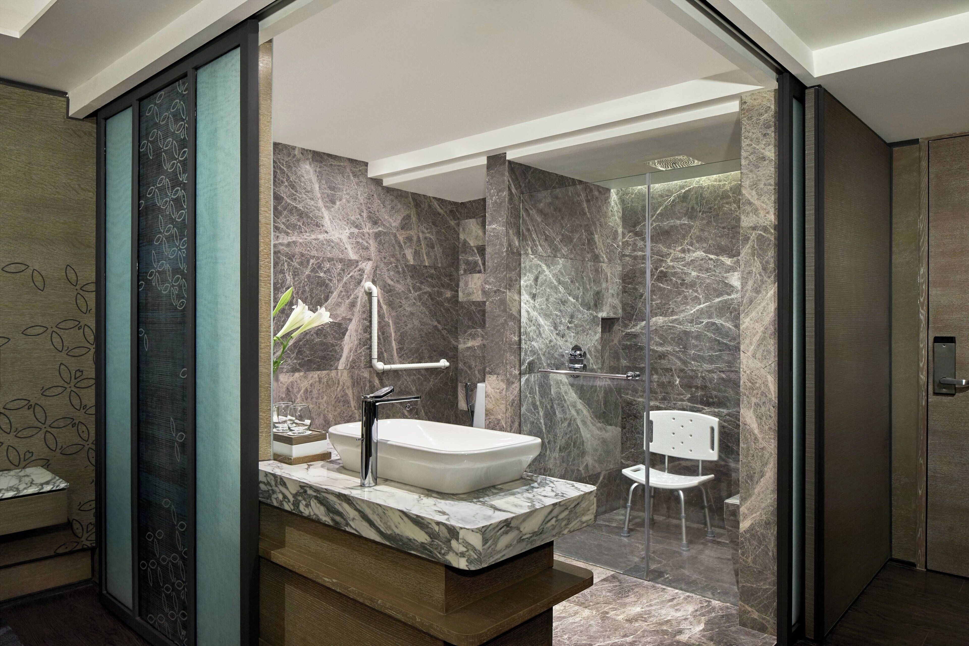 A modern bathroom with a marble sink, glass shower enclosure, and a wooden vanity.