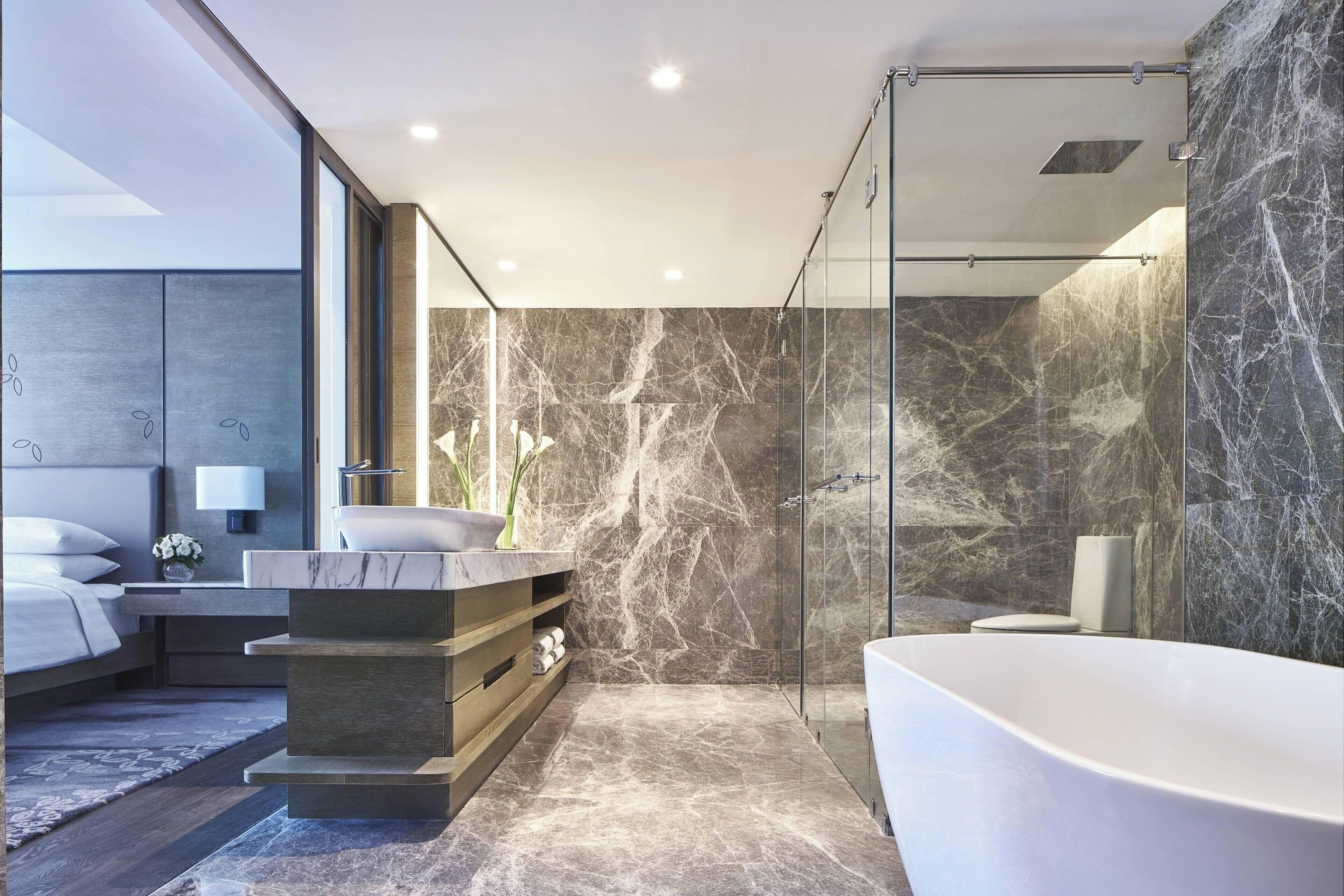 A modern bathroom with a freestanding bathtub, a glass-enclosed shower, and marble walls.