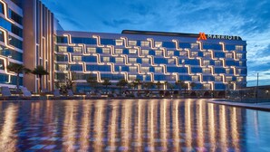 Un hôtel Marriott doté d’une façade moderne, d’un espace piscine avec des chaises longues et d’un ciel dégagé.