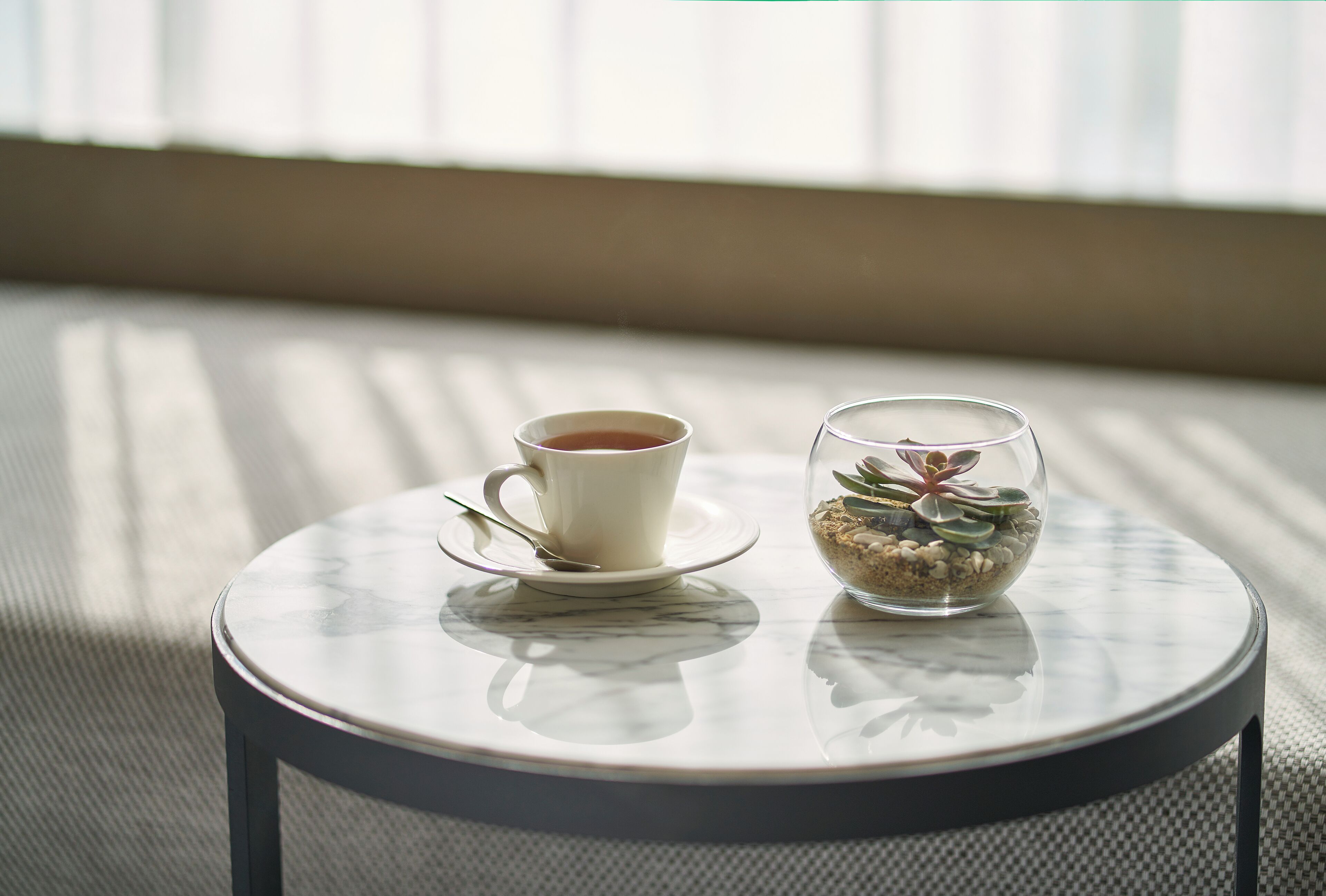 Una mesa redonda con una taza de té y un vaso que contiene una planta jugosa.