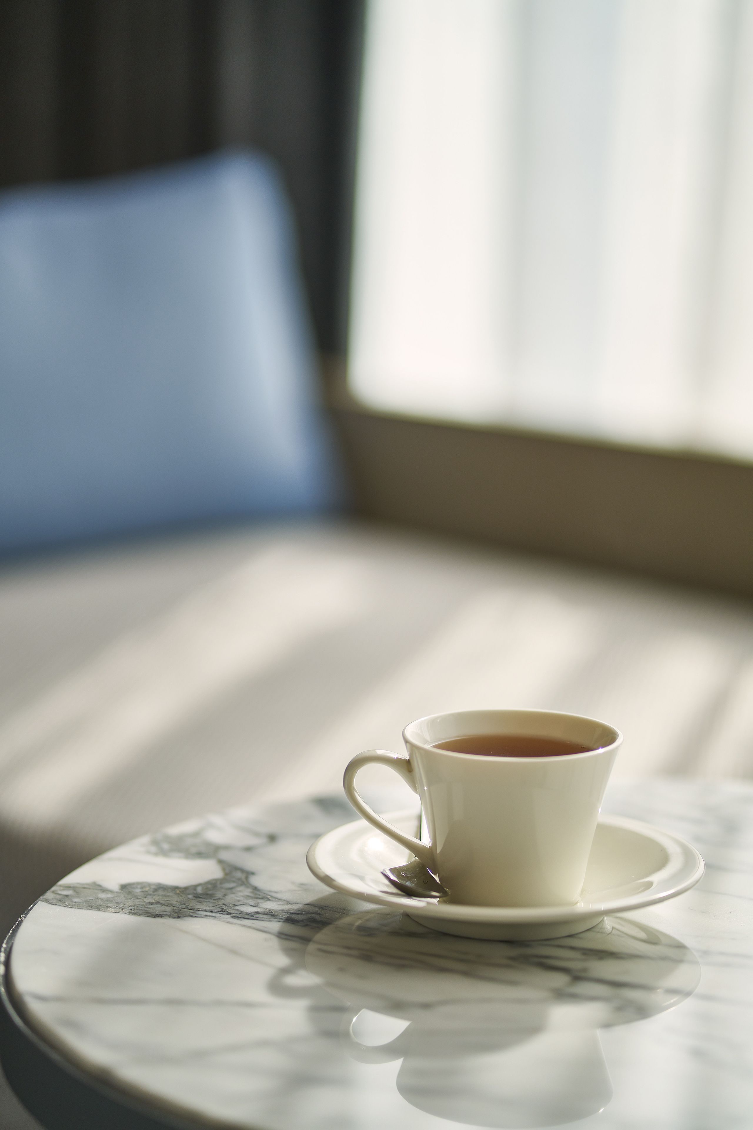 Egy fehér csésze tea egy márvány asztalon, a háttérben egy kék székkel.
