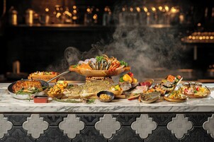 Una variedad de platos sobre una mesa de mármol, incluyendo un pescado asado entero, mariscos y diversas ensaladas.
