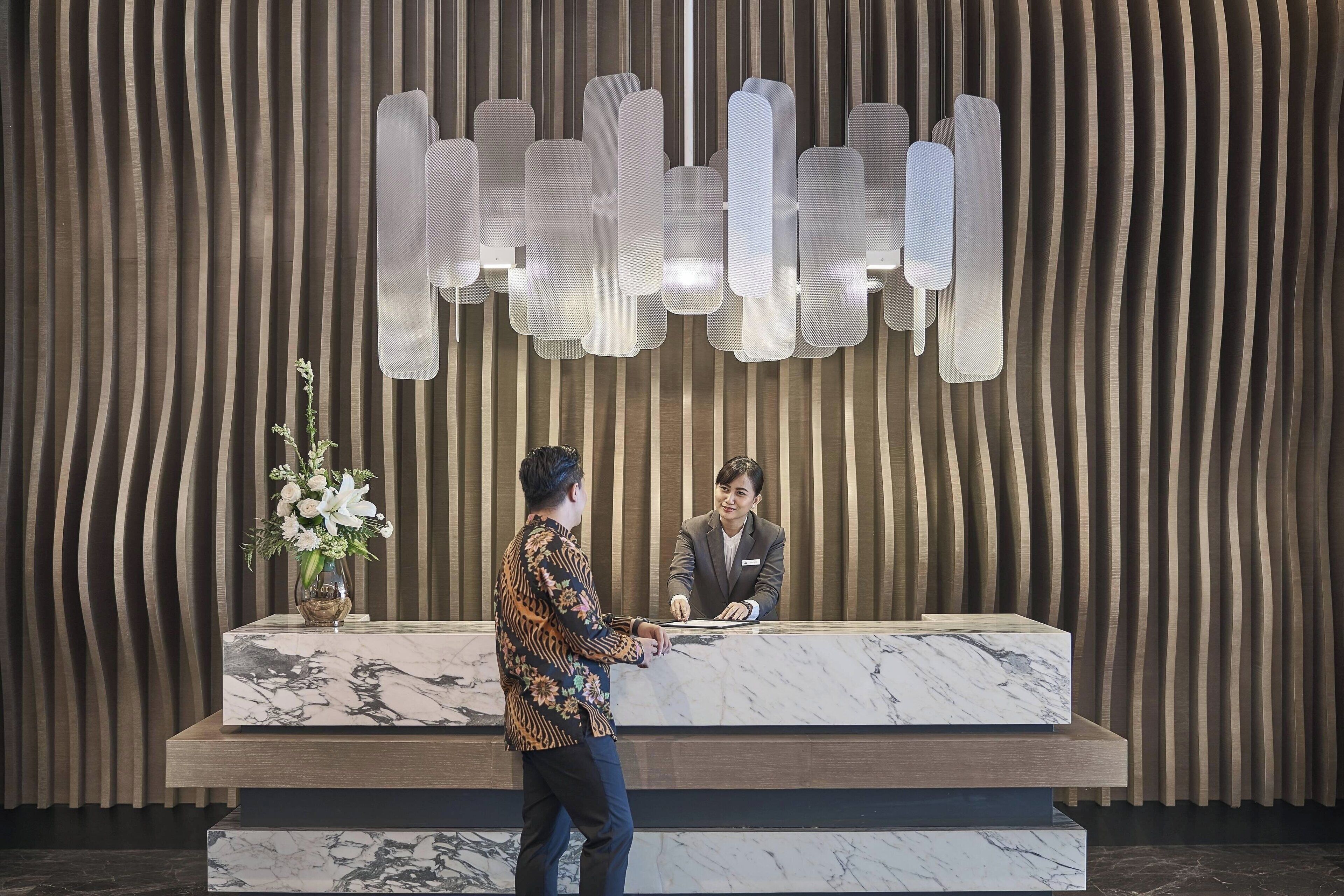 A reception desk with a marble top, a vase of flowers, and a modern light fixture above.
