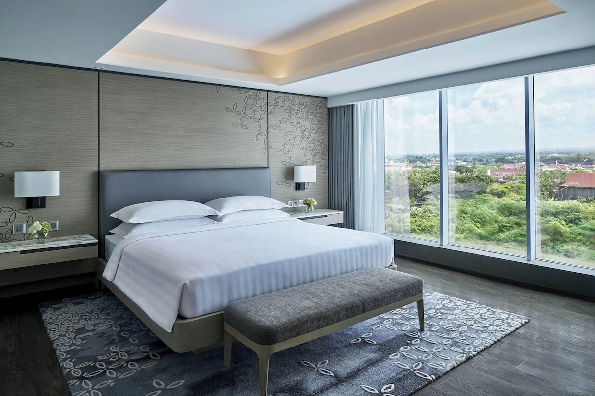 Una habitación de hotel moderna con una cama grande, un banco y vistas a la ciudad.