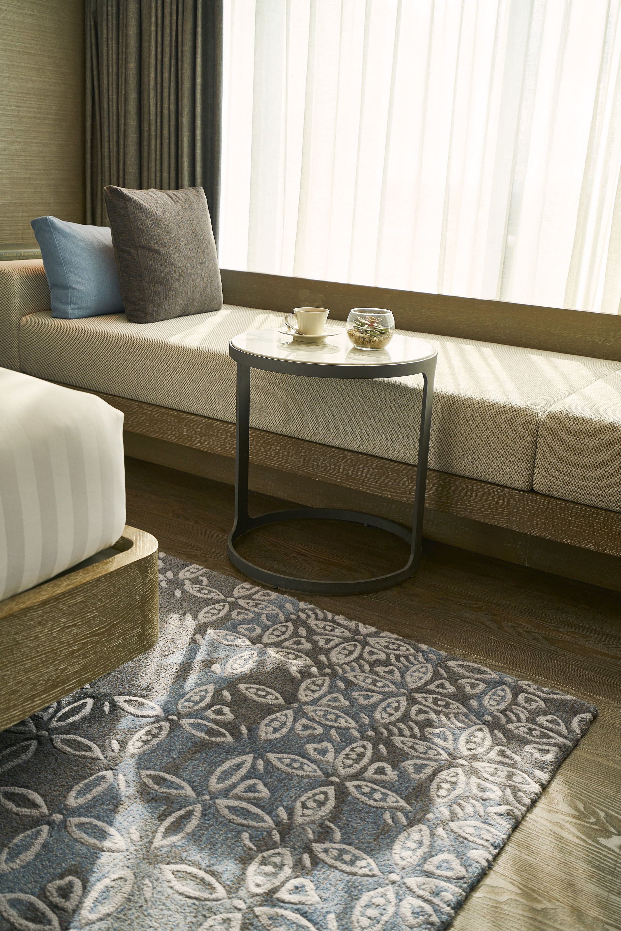 Ein gemütliches Wohnzimmer mit einer Couch, einem kleinen runden Tisch mit Tasse und Glas sowie einem gemusterten Teppich.