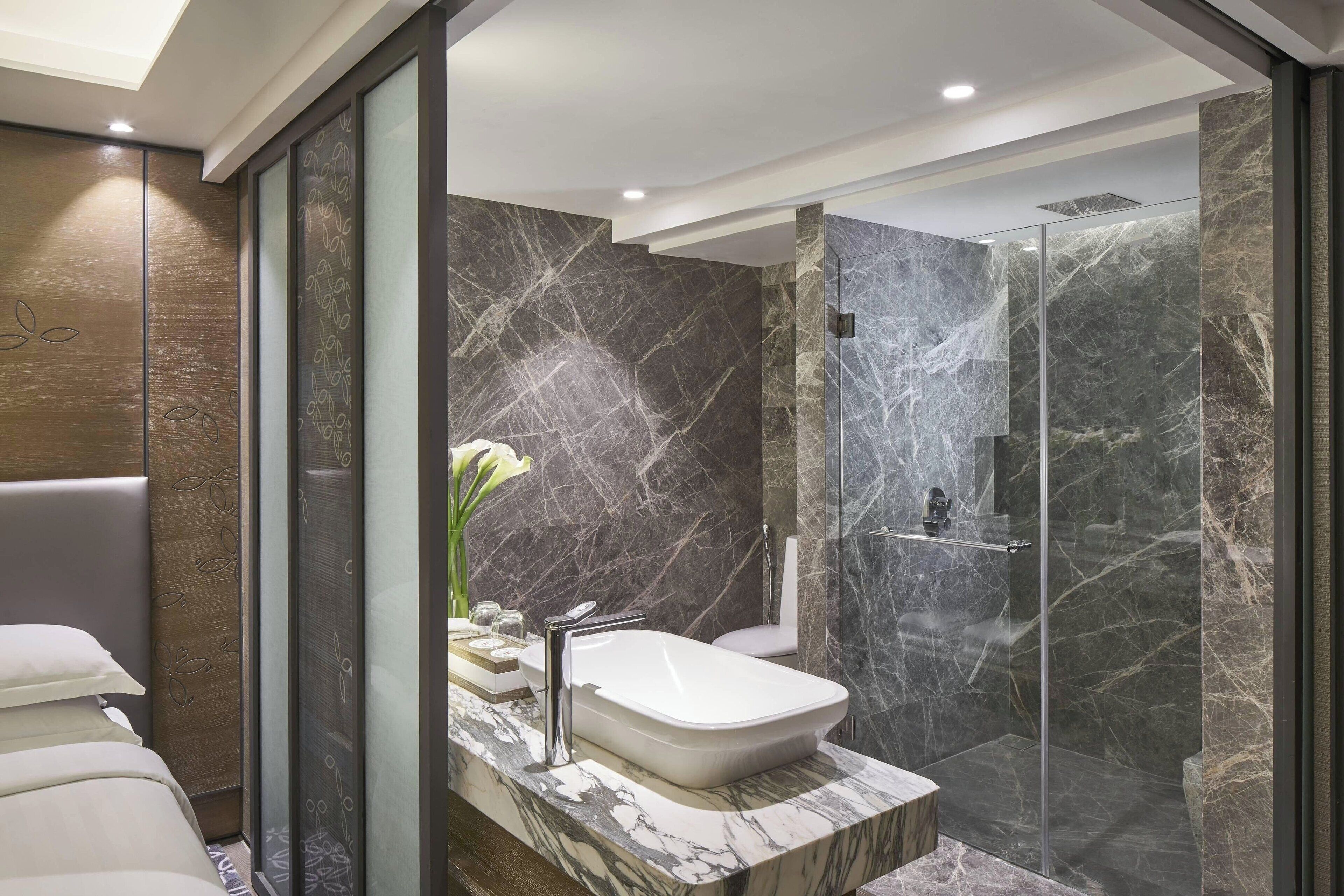 A modern bathroom with a marble sink, a glass shower enclosure, and a toilet.