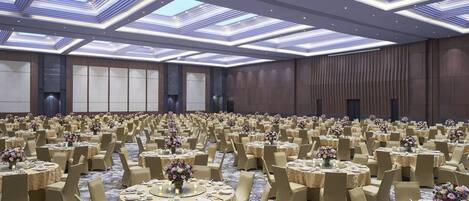 Un amplio salón de banquetes con mesas redondas, sillas color beige y centros de mesa con flores.
