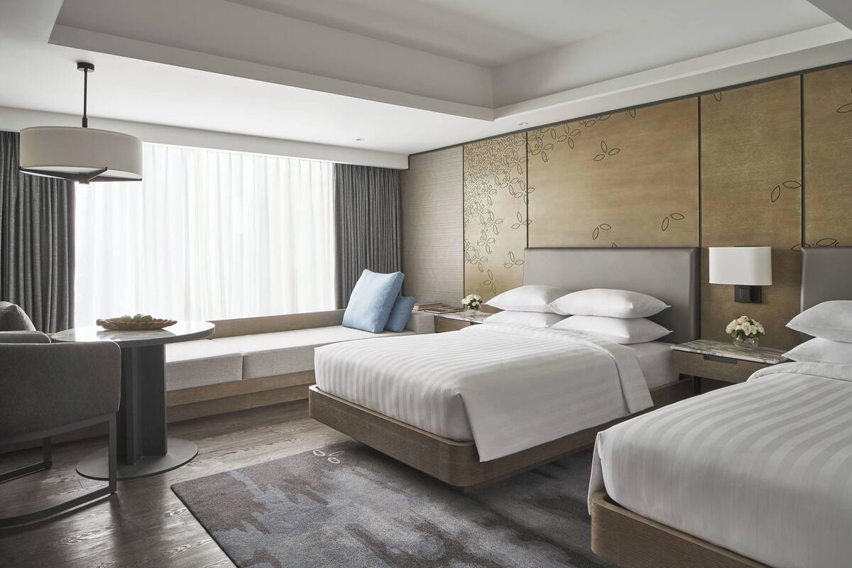 Una habitación de hotel moderna con una cama grande, un sofá, una mesita y una ventana con cortinas.