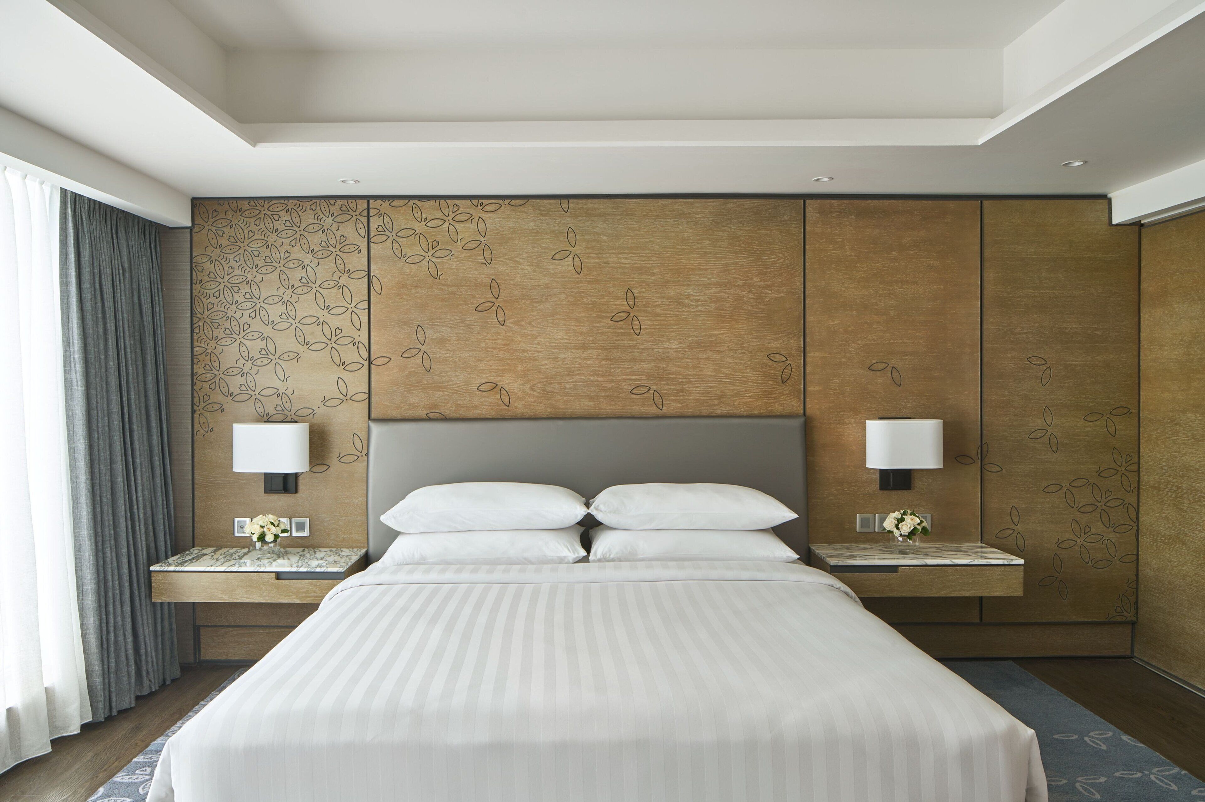 Una habitación de hotel moderna con una cama grande, dos mesitas de noche y una lámpara de pared.