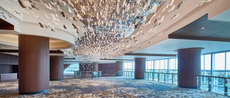 A spacious lobby with a patterned carpet, large wooden columns, and a ceiling with hanging light fixtures.