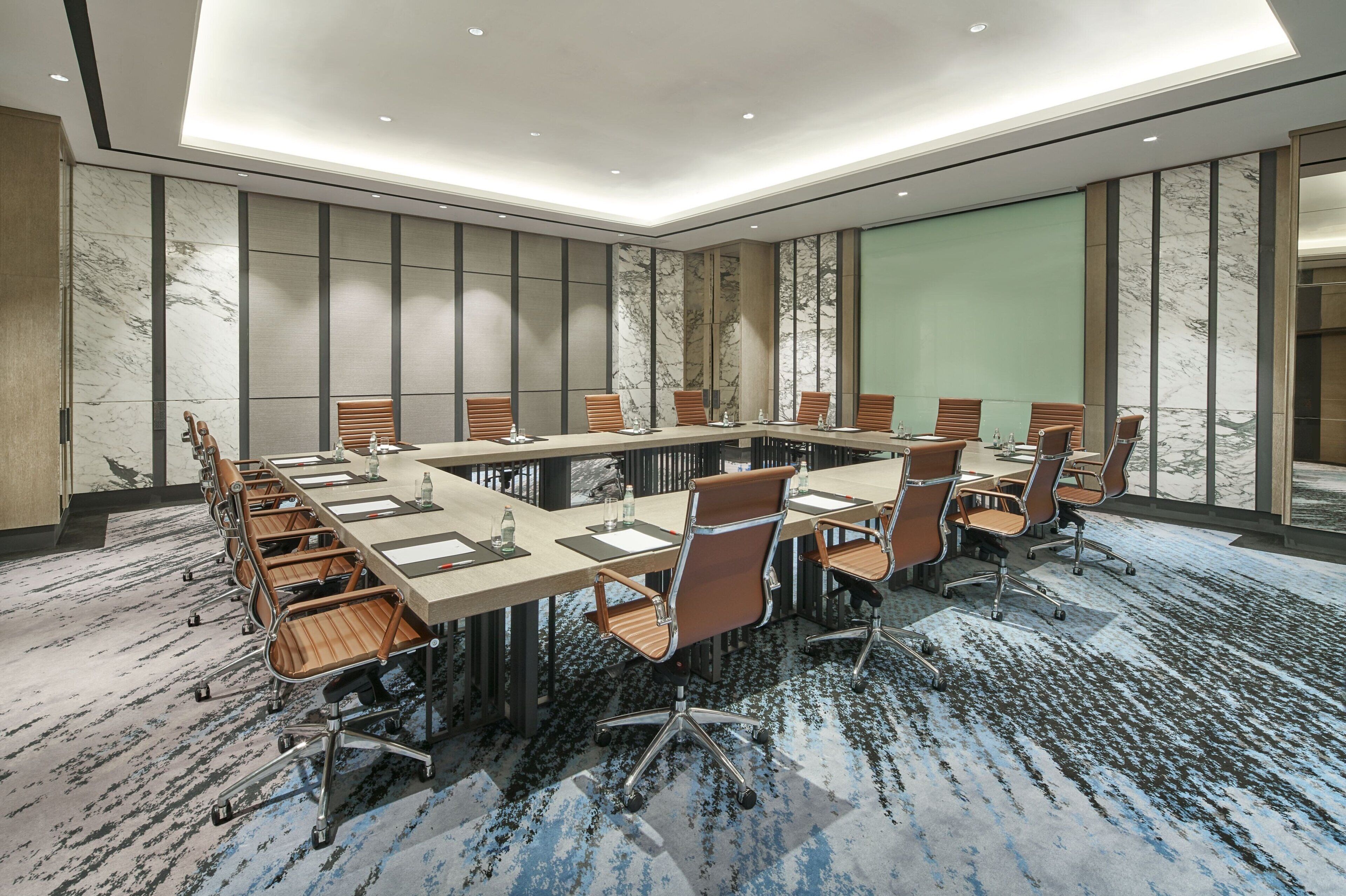 Un salón de conferencias con una larga mesa, varias sillas y una pantalla grande.