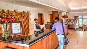 A hotel reception area with a wooden reception desk, a framed certificate, and a vase of flowers. - City Lodge Hotel Durban (Durban)
