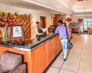 A reception desk with a wooden panel design, a framed certificate, and a vase of flowers. - City Lodge Hotel Durban (Durban)