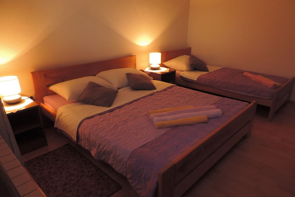 Habitación de hotel con dos camas, cada una con cabecero de madera, una mesita de noche con lámpara y una alfombra estampada.