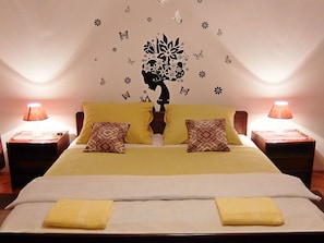 A double bed with two yellow pillows, a decorative wall mural, and two bedside lamps. - Apartments Rendulic (Rakovica)