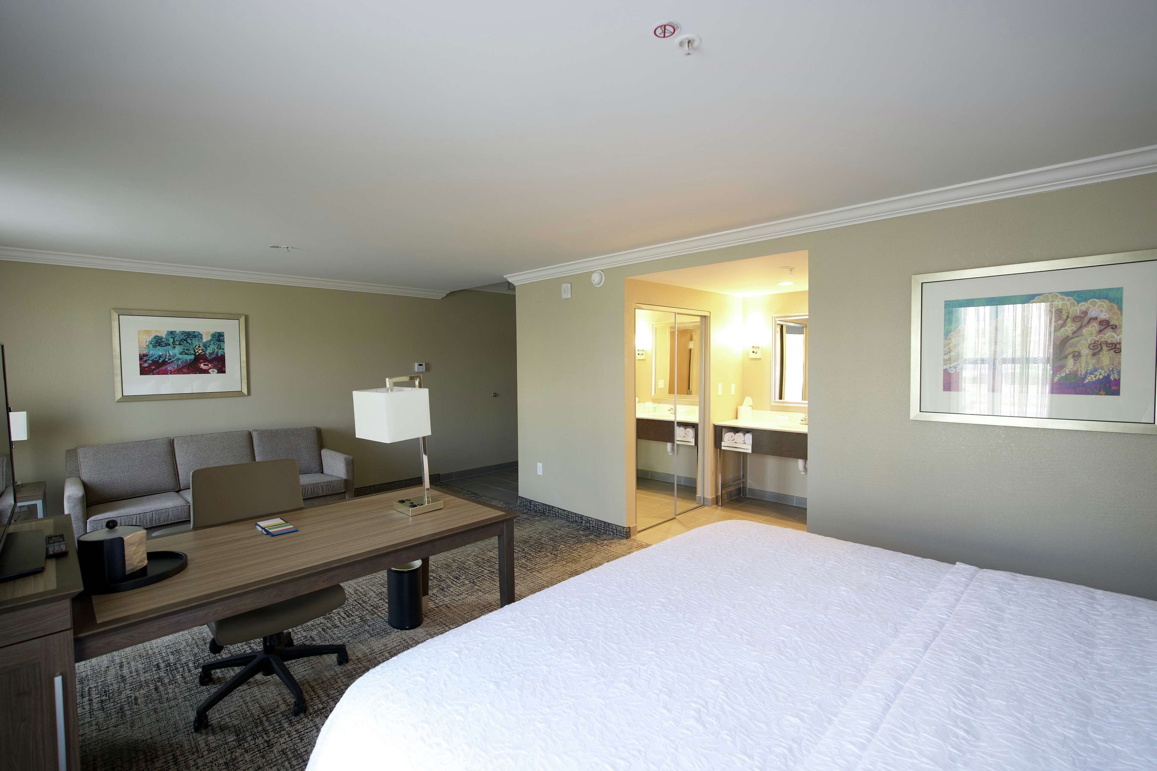 A hotel room with a bed, a desk, a sofa, a lamp, and a painting on the wall.