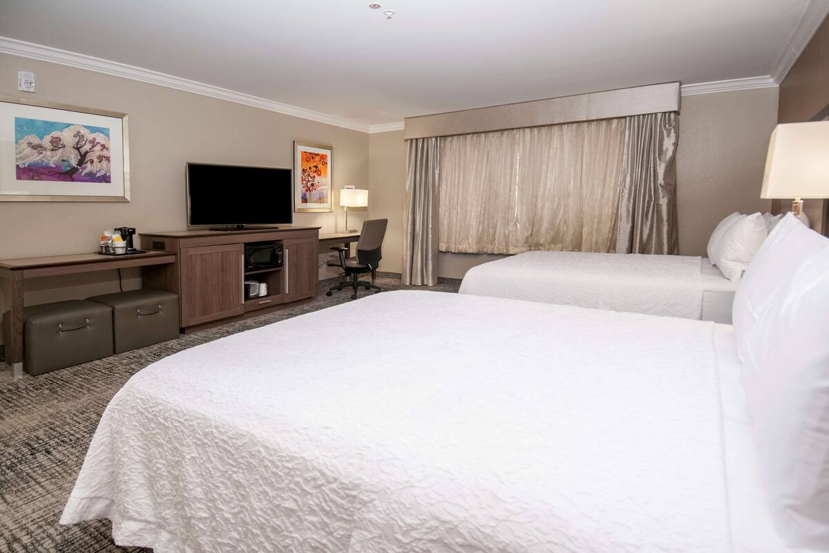 A hotel room with a large bed, a TV, a desk with a chair, and a window with curtains.