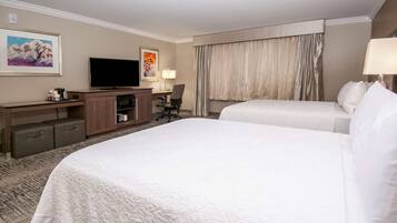 Quarto de hotel com uma cama grande, televisão, escrivaninha com cadeira e janela com cortinas.
