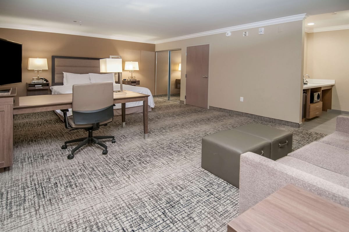 A hotel room with a bed, desk, chair, and a small seating area.