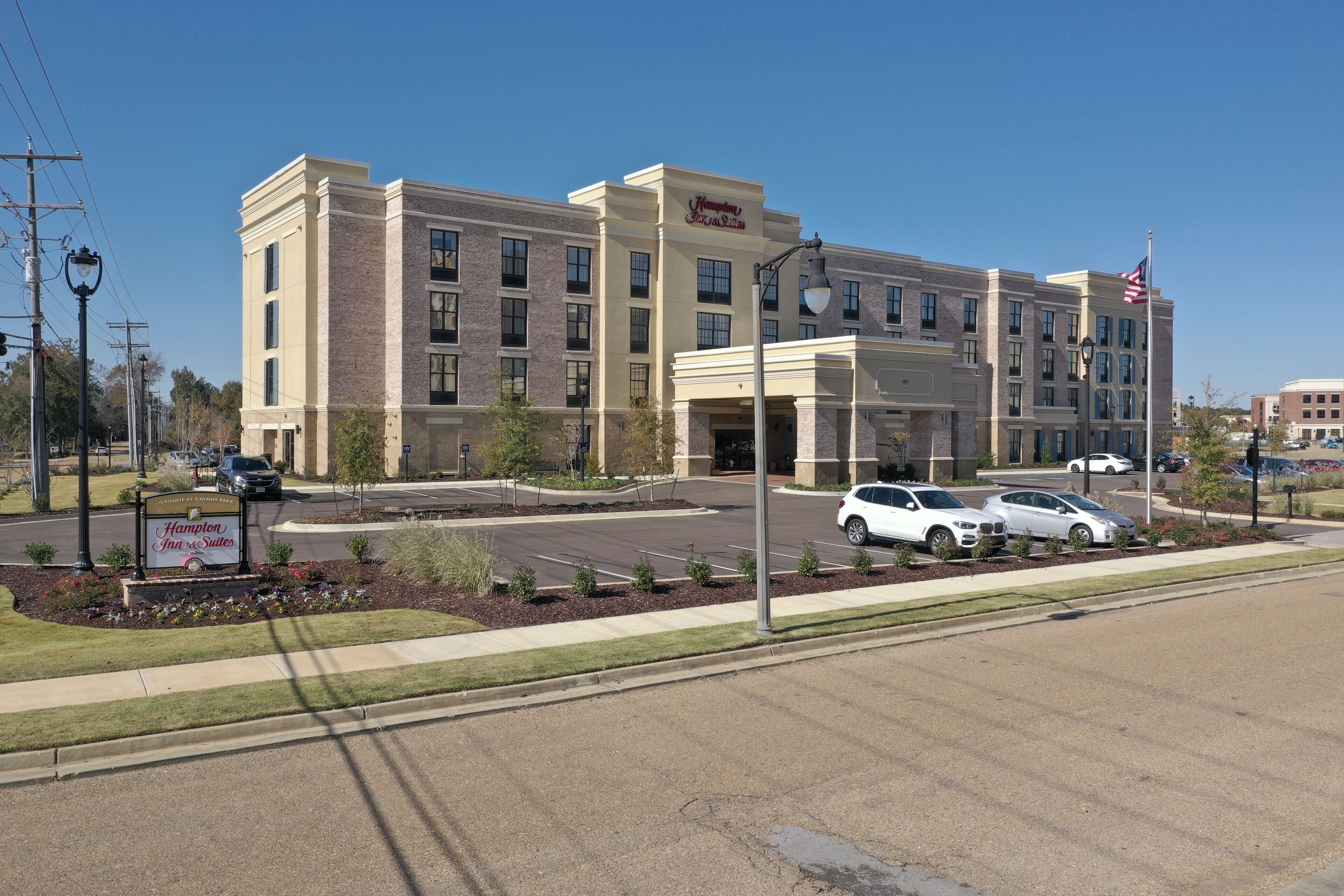 A Hampton Inn & Suites hotel with a brick facade, multiple windows, and a parking lot with several cars.