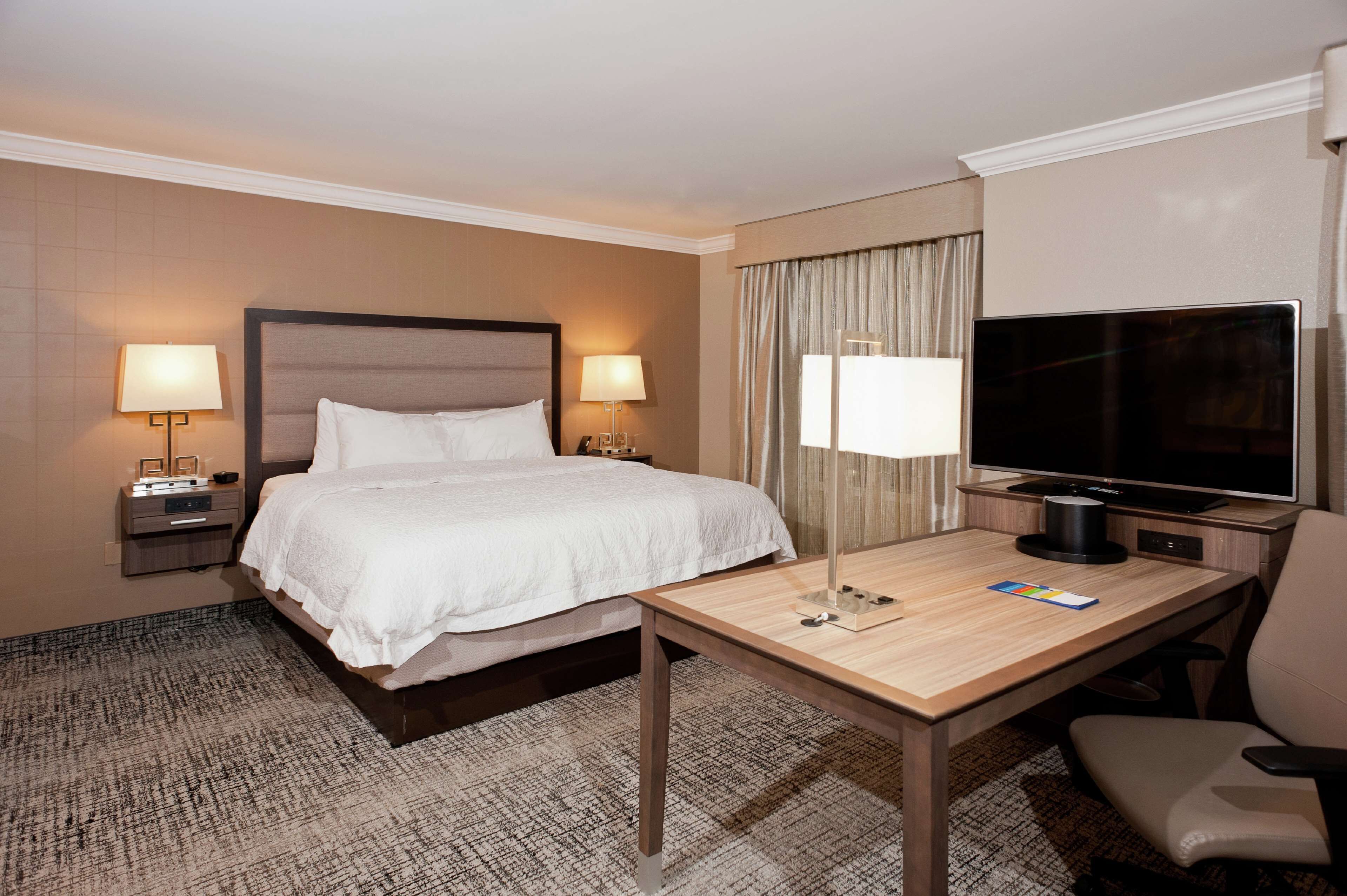 A hotel room with a bed, bedside tables with lamps, a desk with a TV, and a chair.