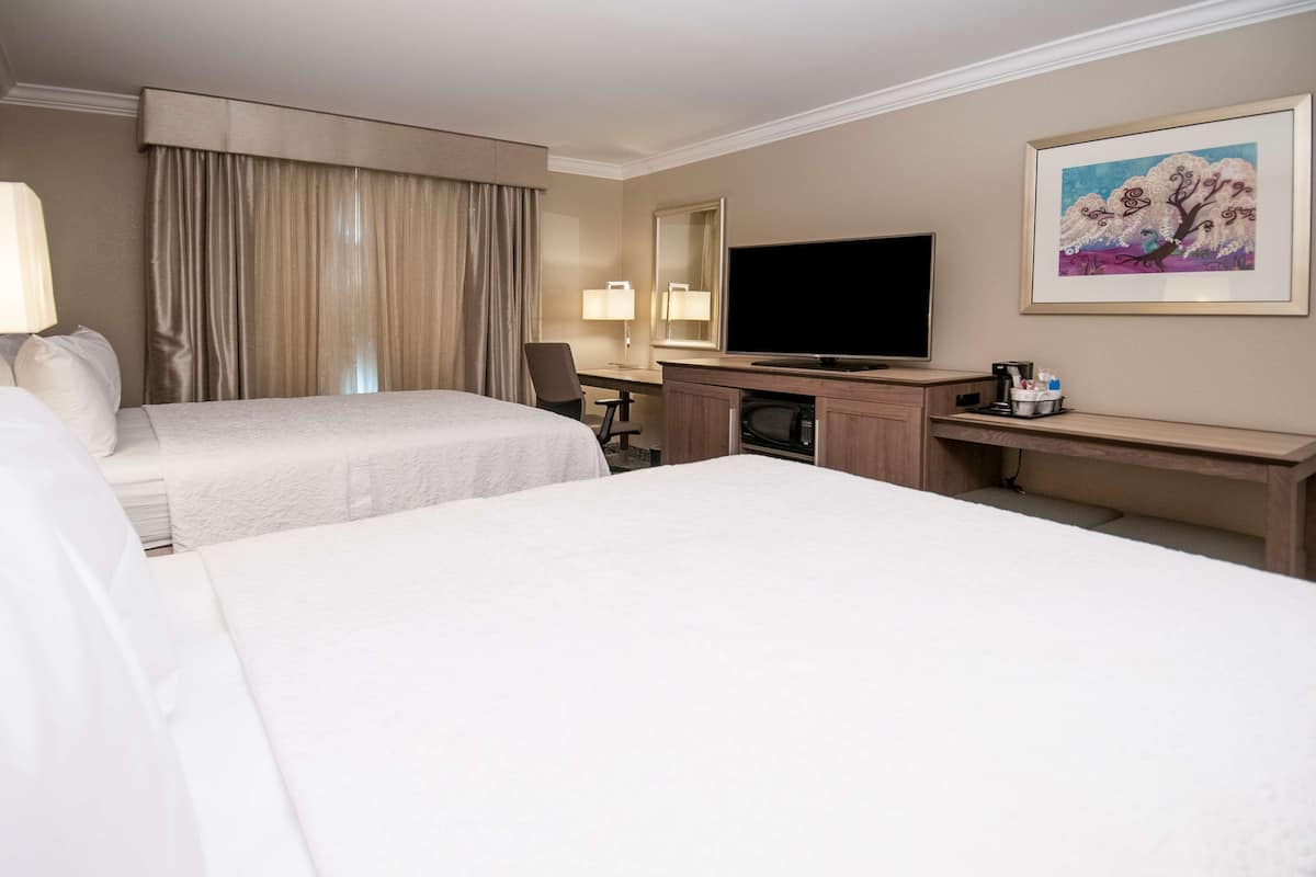 A hotel room with two beds, a desk, a television, and a painting on the wall.