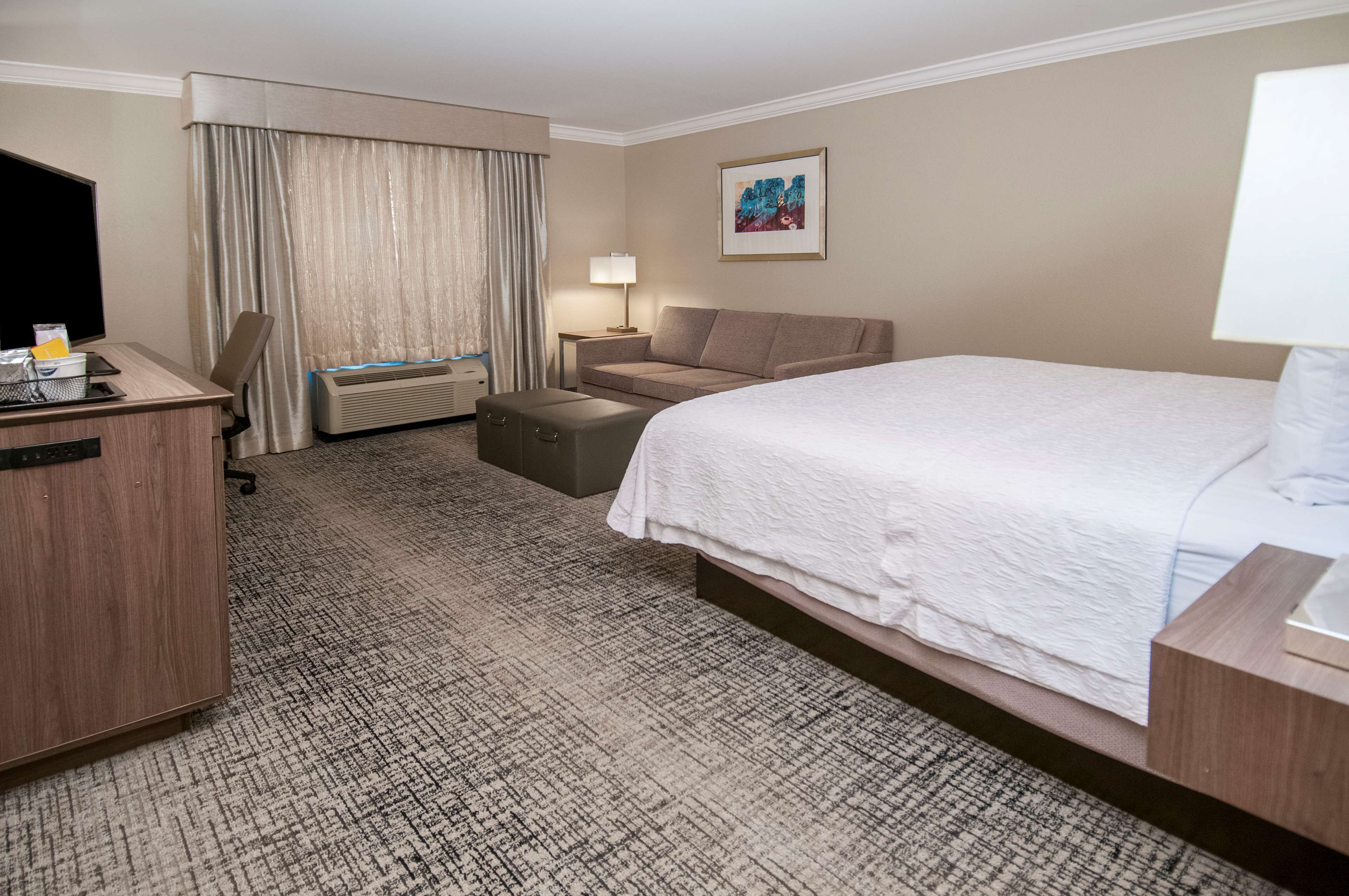 Una habitación de hotel con cama, escritorio, silla, sofá, televisor y lámpara.