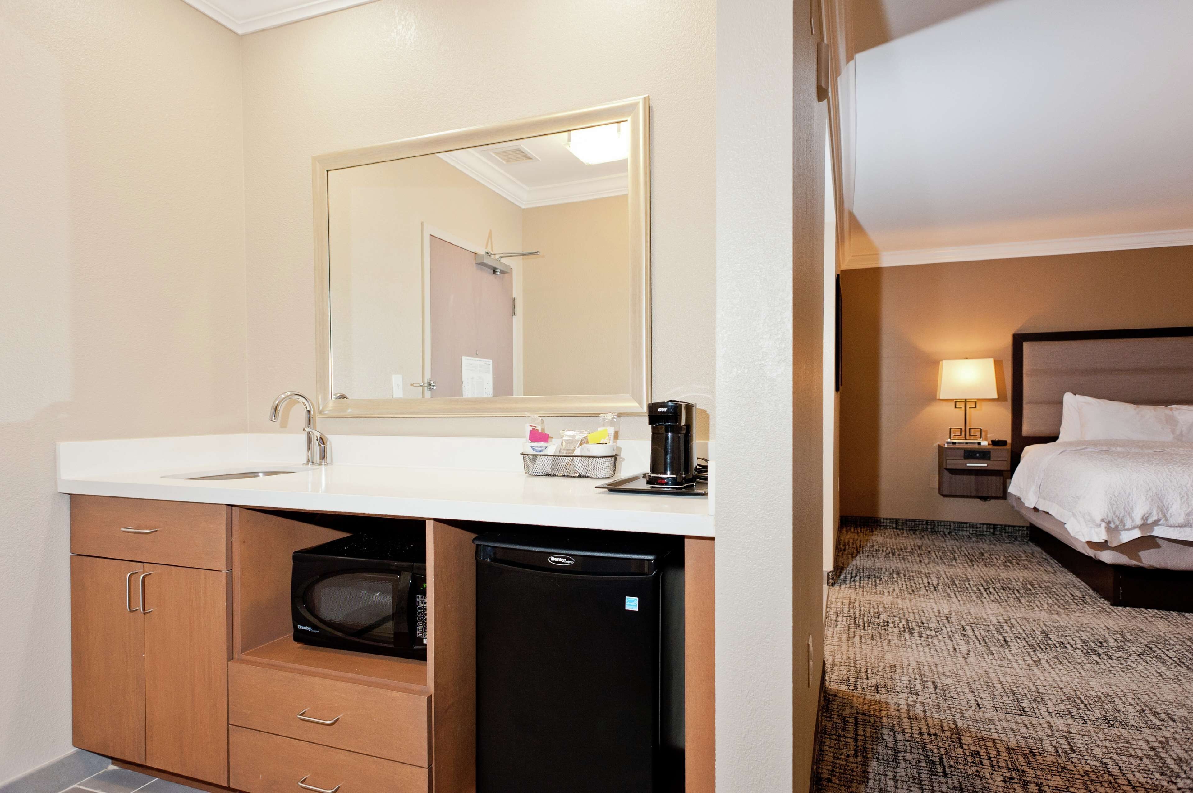 Un baño de hotel con lavamanos, espejo y un refrigerador pequeño.