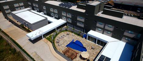 Un hotel moderno con piscina en la azotea, varios pisos y un espacio exterior cubierto.