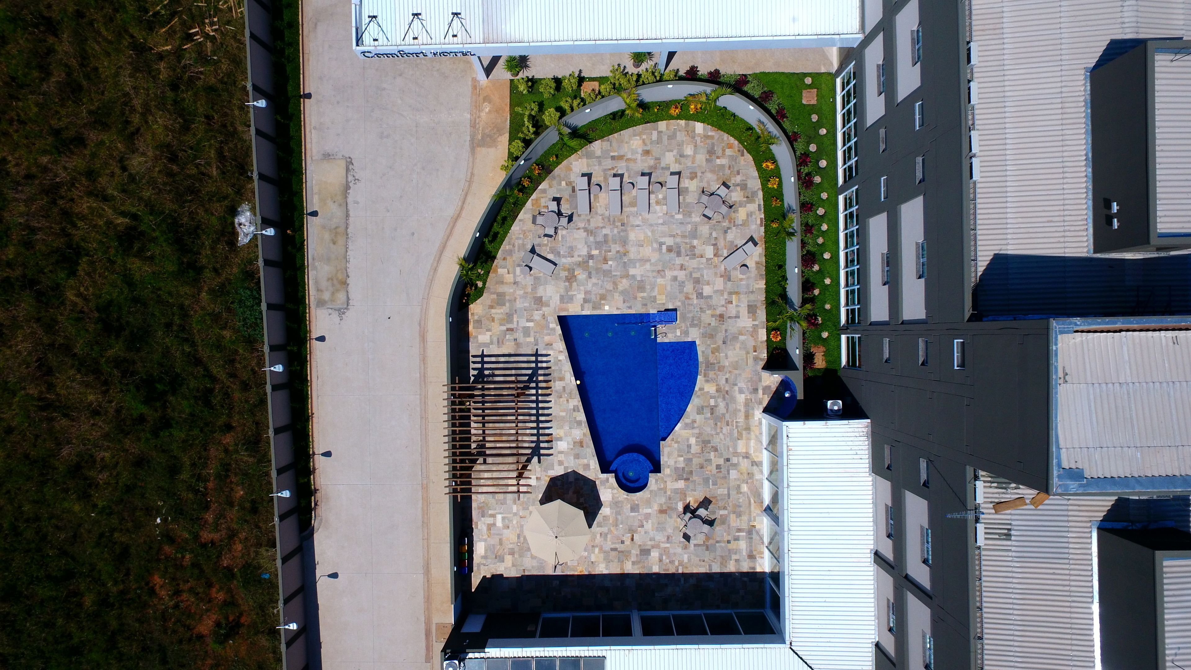 An aerial view of a hotel with a central courtyard, a swimming pool, and a parking area.