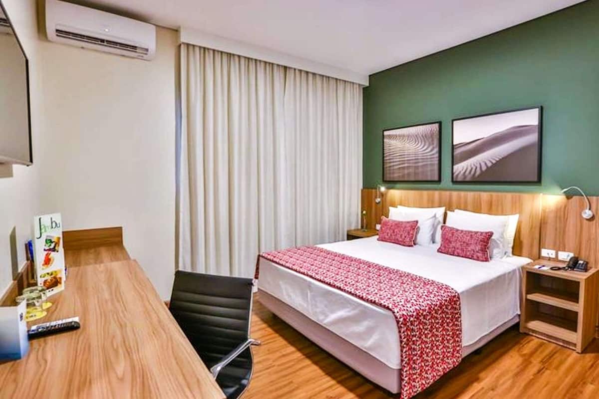 A hotel room with a large bed, a desk, a chair, a nightstand, and two wall-mounted artworks.
