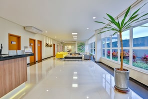 A hotel lobby with a reception desk, yellow seating area, and large windows with a view of the outdoors. - Comfort Hotel Mogi Guaçu (Mogi-Guaçu)