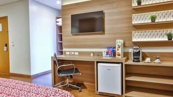 Une chambre d’hôtel moderne dotée d’un bureau en bois, d’un téléviseur à écran plat, d’un mini-réfrigérateur, d’une machine à café et d’un lit recouvert d’une couvre-lit à motifs.