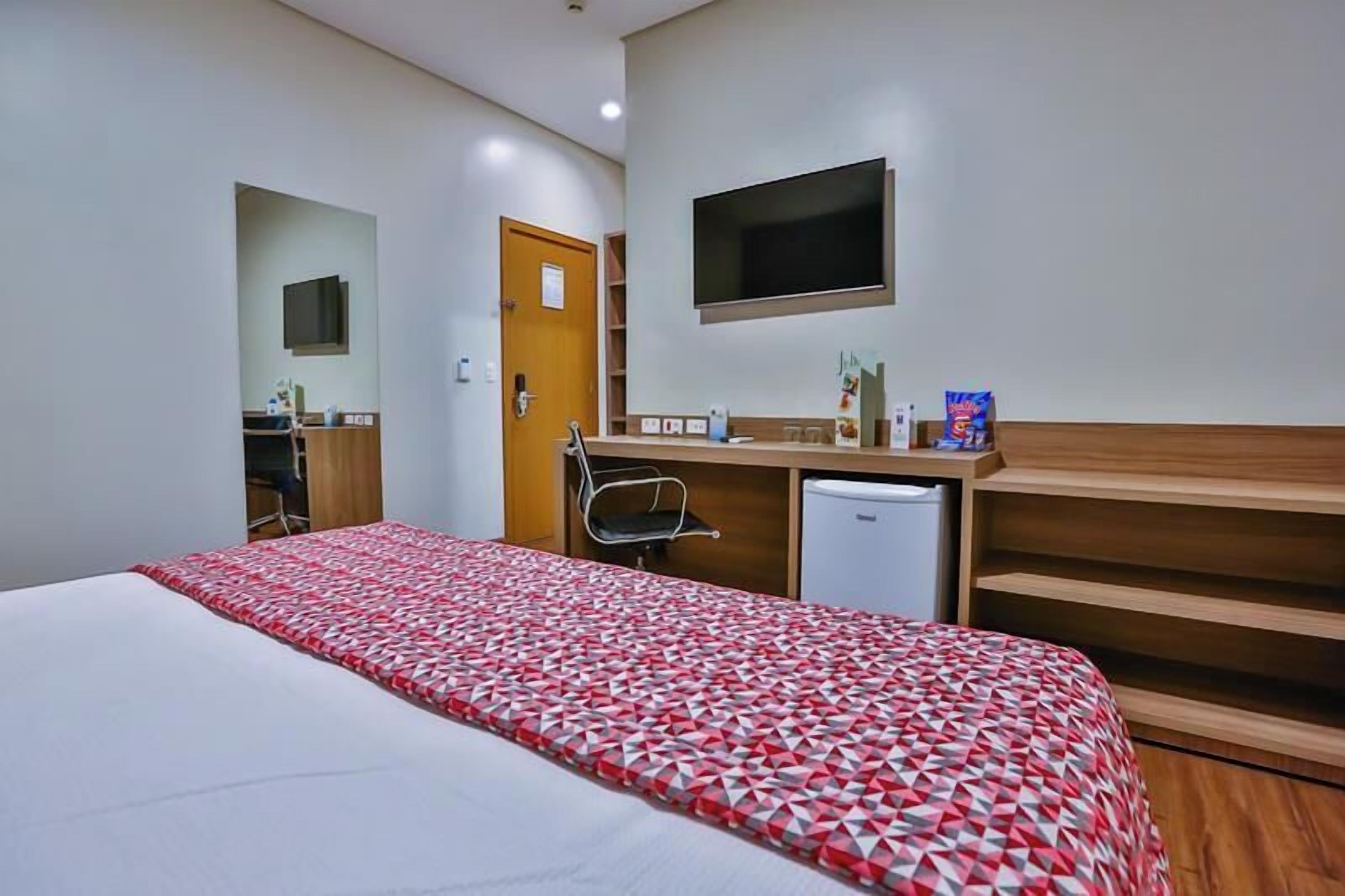 Une chambre d’hôtel équipée d’un lit, d’un bureau, d’une chaise, d’une télévision et d’un petit réfrigérateur.