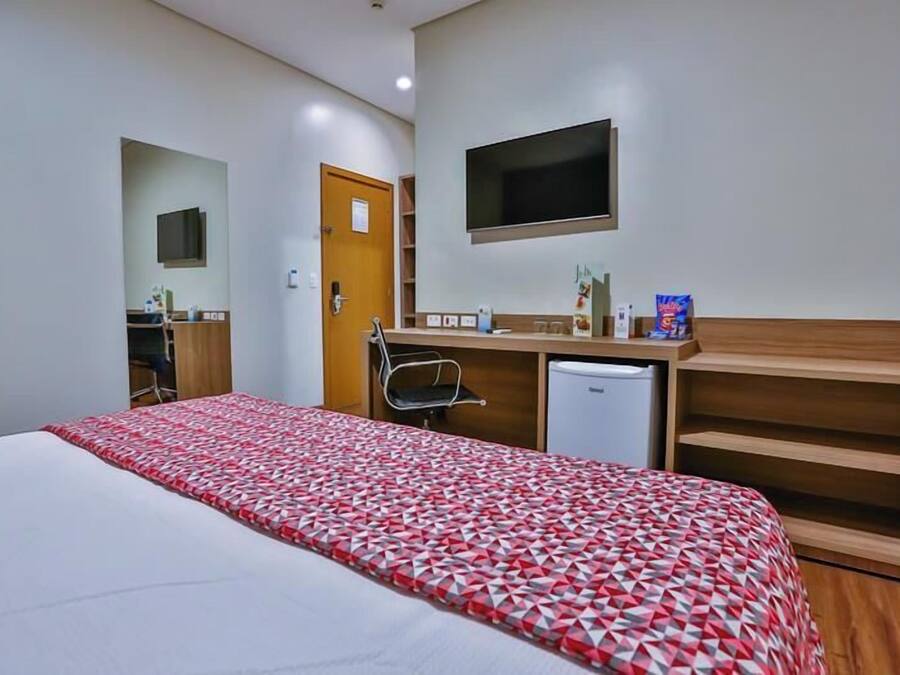 A hotel room with a bed, a desk, a chair, a TV, and a small fridge.