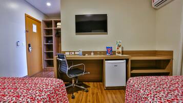 A hotel room with two beds, a desk with a chair, a television, a mini-fridge, and a shelf with towels.